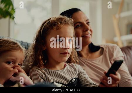 Konzentrierte Mädchen halten Fernbedienung Fernsehen mit Mutter und Schwester zu Hause Stockfoto