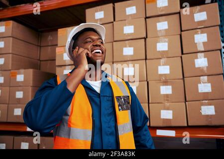 Glückliche Wirtschaftsingenieure sprechen auf dem Handy mit gestapelten Boxen Im Hintergrund Stockfoto