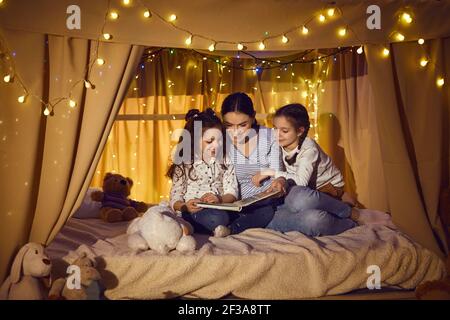 Glückliche Mutter und Kinder sitzen im Spielzimmer Zelt und lesen Buch der Märchen Stockfoto