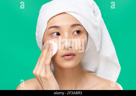 Frau mit einem Handtuch auf dem Kopf wischt ihr Gesicht Mit einem Wattepad Grün Hintergrund Stockfoto