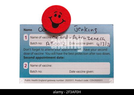 COVID-19-Impfkarte, ausgestellt vom NHS für Oxford AstraZeneca-Impfstoff, Oxford Astra Zeneca-Impfstoff mit Smiley-Face-Emoji-Aufkleber Stockfoto