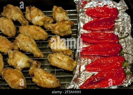 Gebackene Flügel in Semmelbröseln und gebackener Paprika auf Aluminiumfolie. Alles wird auf ein spezielles Backblech für den Backofen gestellt. Stockfoto