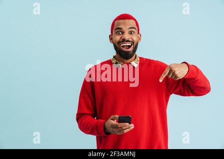 Aufgeregt afroamerikanischen Kerl mit und zeigen Finger auf Handy Isoliert auf blauem Hintergrund Stockfoto