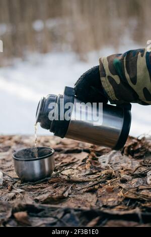 Mann gießt einen heißen Tee aus einer Thermoskanne in ein becher im Freien Stockfoto