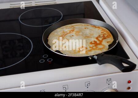 Ein Pfannkuchen wird in einer Pfanne auf einem gebraten Elektroherd Stockfoto