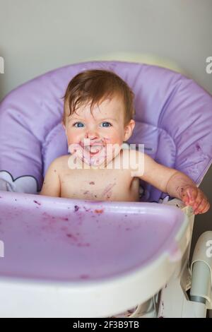 Adorable Baby essen auf Babystuhl und machen ein Durcheinander. Kleines Mädchen essen Essen in der Küche. Stockfoto