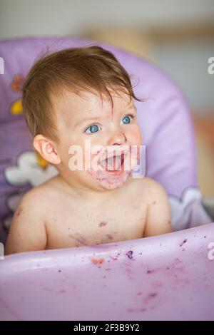 Adorable Baby essen auf Babystuhl und machen ein Durcheinander. Kleines Mädchen essen Essen in der Küche. Stockfoto