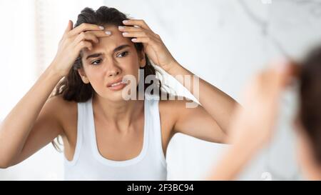 Traurige Frau Mit Akne Problem Quetschen Pickel Auf Stirn Indoor Stockfoto