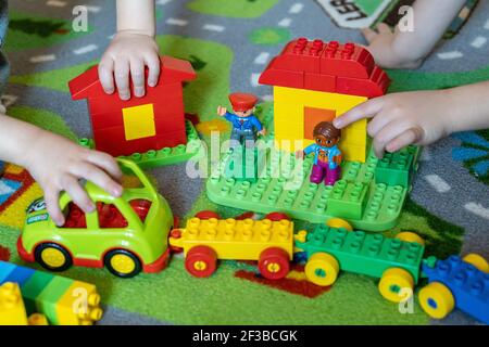 Nahaufnahme von Kinderhände, die mit bunten Plastikziegeln auf einem bunten Teppich spielen. Stockfoto