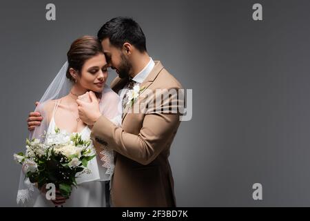 Eleganter arabischer Mann umarmt Frau im Hochzeitskleid auf grau Stockfoto