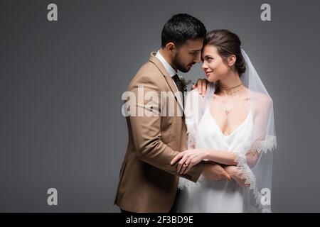 Glückliches multiethnisches frisch vermähltes Paar, das sich isoliert ansieht Grau Stockfoto