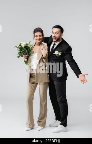 Aufgeregt arabischen Mann gesturing in der Nähe Braut zeigt Ehering auf Grau Stockfoto