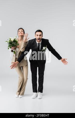 Aufgeregt Braut zeigt Ehering in der Nähe erstaunt muslimischen Verlobten stehen Mit offenen Armen auf grau Stockfoto