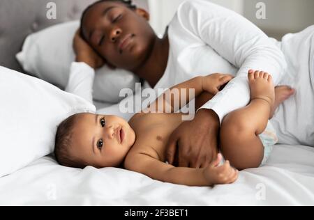 Nette kleine afrikanisch amerikanische Baby schlafen im Bett mit Mutter