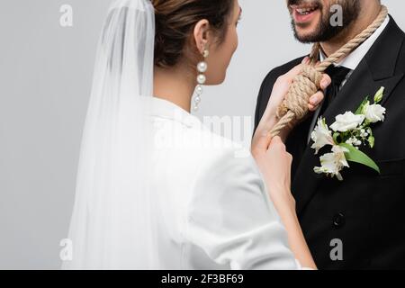 Junge Braut trägt Slip Knoten am Hals des Bräutigams isoliert Auf Grau Stockfoto