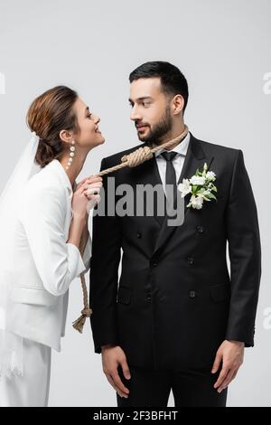 Lächelnde Braut zieht Slip Knoten am Hals des arabischen Bräutigam Isoliert auf Grau Stockfoto
