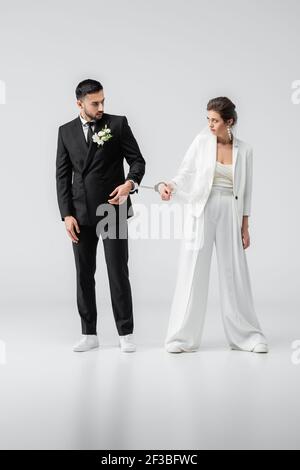 Multiethnische Jungvermählte in Handschellen, die sich auf weiß angucken Hintergrund Stockfoto