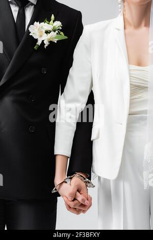 Verkürzte Ansicht von Braut und Bräutigam mit Händen in Handschellen Isoliert auf Grau Stockfoto