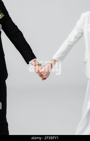 Verkürzte Ansicht von Braut und Bräutigam in Handschellen halten Hände Isoliert auf Grau Stockfoto