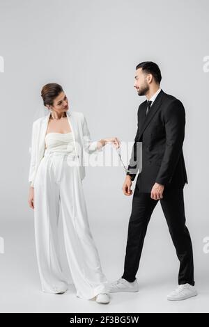 Braut im Hochzeitsanzug mit Handschellen von muslimischen Freund auf Weißer Hintergrund Stockfoto