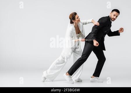 Arabischer Mann in formeller Kleidung und Handschellen in der Nähe der Braut laufen Auf weißem Hintergrund Stockfoto