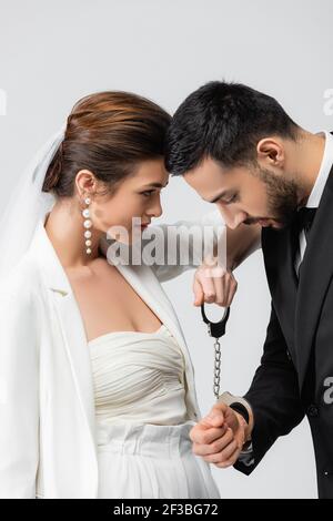 Braut hält Handschellen in der Nähe verärgert muslimischen Bräutigam isoliert auf grau Stockfoto