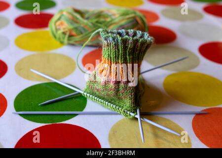 Grüne und orange Socke, die auf 4 Stricknadeln gestrickt wird Auf einem Öltuch Tischtuch Tischdecke orange grün gelbe Kreise UK KATHY DEWITT Stockfoto