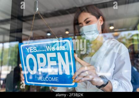 Coffee Shop asiatische Frau Besitzer mit Gesichtsmaske, nach Sperrung Quarantäne im Café covid-19 verhindern geöffnet. Stockfoto