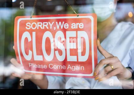 asiatische Frau trägt Schutz Gesichtsmaske Drehen geschlossen Schild an Glastür für offene Café Restaurant nach Coronavirus oder covid-19 Quarantäne. Re Stockfoto