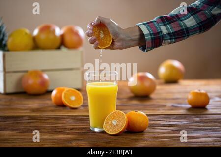 Weibliche Hand drückt frische Orange auf das Glas auf Holz Tabelle Stockfoto