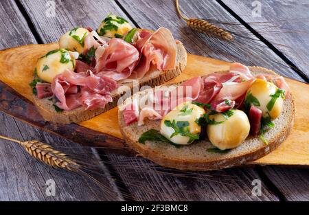 Snack-Vorspeise mit Vollkornbrot, rohem Schinken und geräucherten Provola-Kugeln in Öl Stockfoto