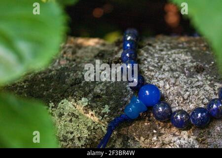 Nahaufnahme von blauen mala Perlen auf Stein zwischen grünen Blättern. Buddhistische Gebetsperlen für die Japa-Meditation Stockfoto