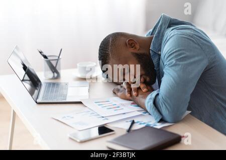 Müde afroamerikanische Freiberufler Kerl schlafen am Schreibtisch mit Laptop Und Papiere Stockfoto