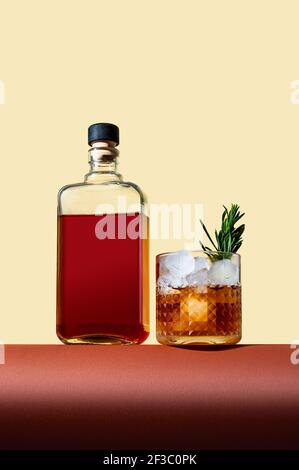 Flasche und Glas mit Whiskey und Eis auf braunem Tisch auf hellem Hintergrund. Moderner Stil. Kreatives Konzept. Stockfoto