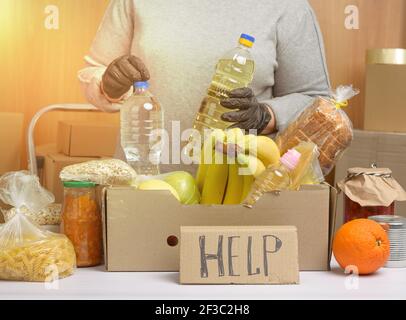 Frau in einem grauen Pullover verpackt Lebensmittel in einem Karton, das Konzept der Hilfe und Freiwilligenarbeit, Spende Stockfoto