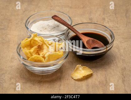 Getrocknete Scheiben von Yacon Knolle, Sirup und Pulver in kleinen Glasschalen gegen handgemachtes Rindenpapier. Yacon enthält Inulin, ein komplexer Zucker, der fördert Stockfoto