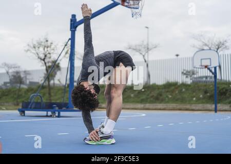 Ein junger energischer Mann lehnt sich nach vorne mit seinem Rücken gerade Und seine linken Füße mit der rechten Hand berühren Stockfoto