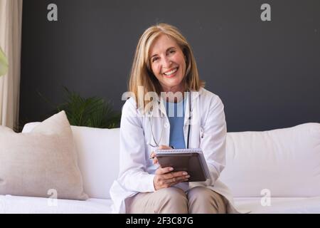 Kaukasische ältere Ärztin sitzt auf dem Sofa lächelnd und gibt Video Rücksprache anrufen Stockfoto