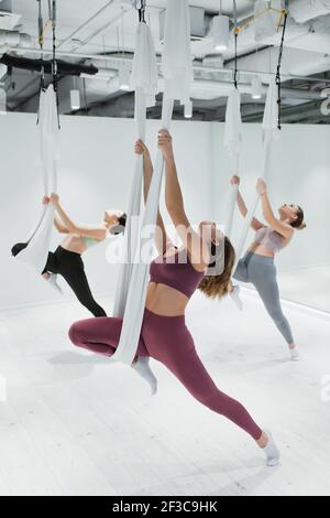 Sportliche junge Frauen, die sich in Fitness auf Yoga-Hängematten ausdehnen Zentrieren Stockfoto