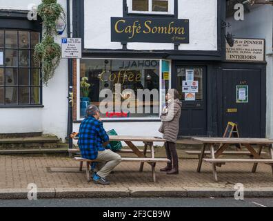 Ein Paar saß an einem Gehsteig Tisch im Gespräch mit einer stehenden Frau trägt eine Gesichtsmaske vor dem Cafe Sombra Café, High Street, Pinner. Stockfoto