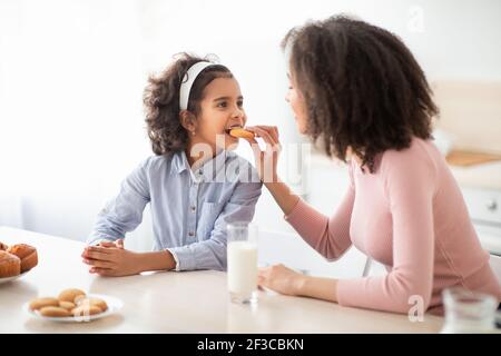 Fröhliche afroamerikanische Frau Fütterung Mädchen mit Cookie Stockfoto