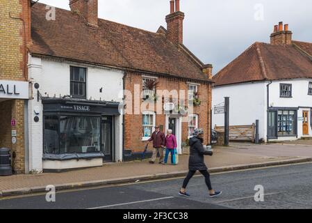 Ältere Männer und Frauen, die in der Pinner High Street spazieren. Junge Frau, die ein Tablett mit Kaffee zum Mitnehmen trägt, kreuzt die Straße. Pinner, Middlesex, England, Großbritannien. Stockfoto