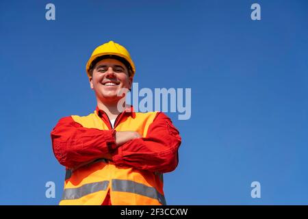 Selbstbewusster junger Arbeiter in reflektierender Kleidung und gelber Hardhat. Portrait eines lächelnden Bauarbeiters oder Ölarbeiters in persönlicher Schutzausrüstung. Stockfoto