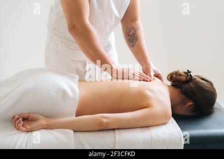 Seitenansicht des männlichen Masseurs, der im Spa-Salon eine Rückenmassage für eine junge, unkenntlich gebliebene Frau macht. Stockfoto