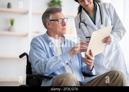 Positive Ärztin, die behinderten älteren Mann anbietet, eine Versicherung zu unterzeichnen Vertrag zu Hause Stockfoto
