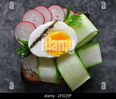 Eiertoast mit Gurke, Sahne Сheese und Roggenbrot auf dunklem Hintergrund. Konzept für gesunde Ernährung.Draufsicht.Nahaufnahme Stockfoto