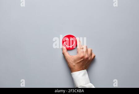 Geschäftsmann Hand hält ein rotes Abzeichen mit einem lächelnden Gesicht Symbol. Kundenzufriedenheit oder positives Feedback-Konzept. Stockfoto