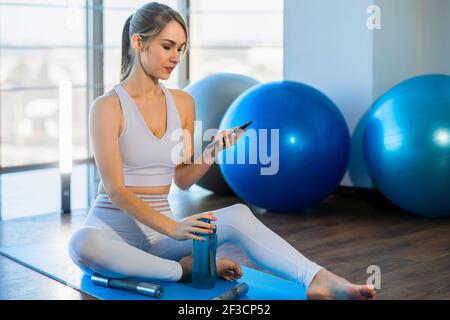 Schöne Frau in Sportswear nach dem Training sitzt auf Yoga Und nutzt das Telefon Stockfoto