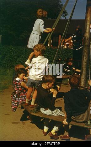 1966, historisch, Sommerzeit und mehrere kleine Kinder sitzen und stehen auf einem Spielplatz Fahrt des Tages, die Witch's hat, England, Großbritannien, mit einem Jungen genießen einen Eiscreme-Wafer. Diese Spielplatzfahrt aus Holz/Metall, die vor über 100 Jahren erfunden wurde, war ein großer Spaß für Kinder unterschiedlichen Alters, da man auf ihr stehen oder sitzen konnte, während sie herum ging, Aber als der große Bruder von Gesundheit und Sicherheit begann zu wachsen, wurde die Fahrt eventallly verboten, da es als zu gefährlich angesehen wurde. Stockfoto