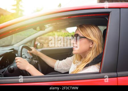 Glückliche schöne Frau fährt ein rotes Auto. Stockfoto